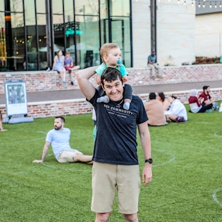 A father carries his child on his shoulders at an outdoor event in College Station, TX